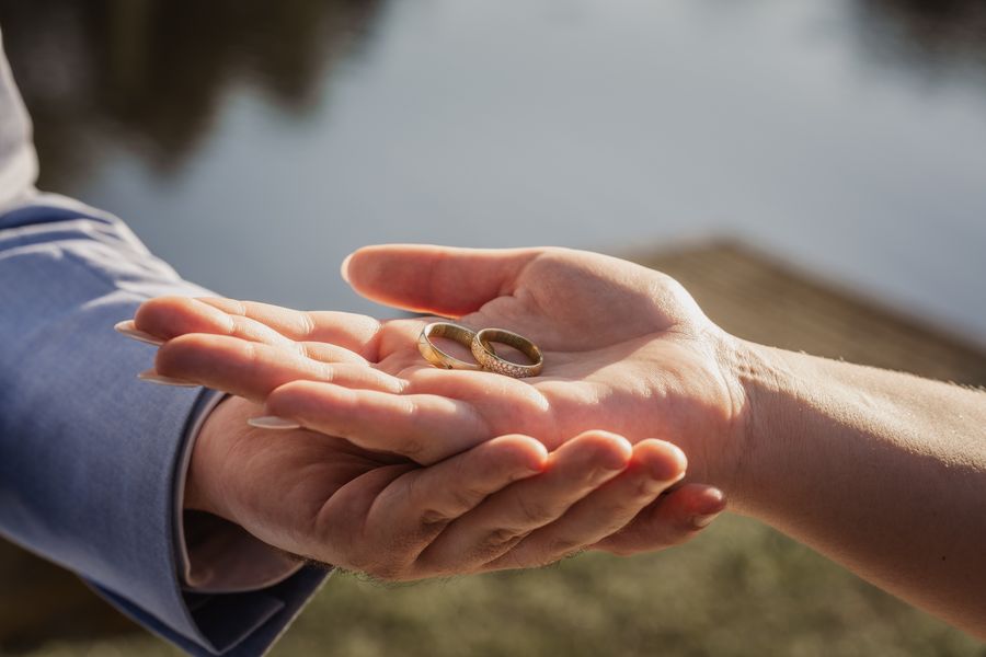 Die beiden Eheringe liegen in Jessicas und Jonas’ Händen, im Hintergrund das Wasser