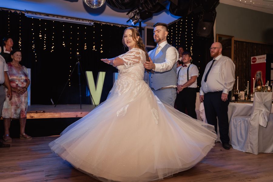 Jessica und Jonas beim Hochzeitstanz, ihr Kleid schwingt, die Gäste schauen zu