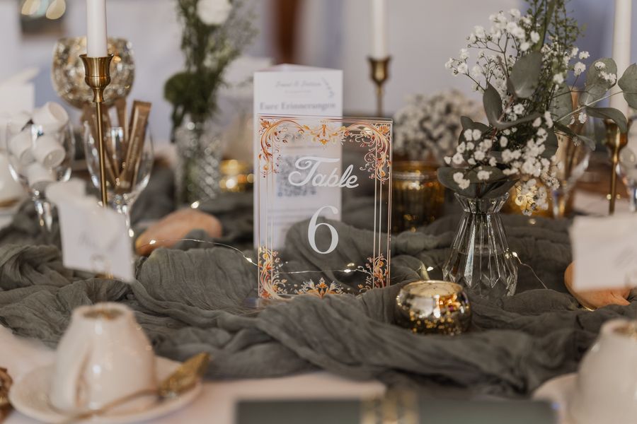 Tischdekoration mit Tischnummer 6, goldenen Kerzenständern, Schleierkraut und Eukalyptus