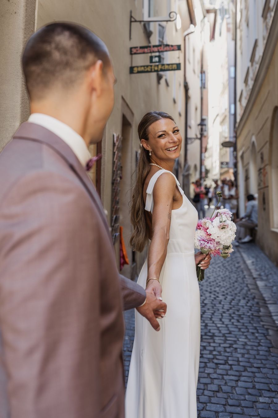 Anna dreht sich in einer Altstadtgasse in Regensburg lachend zu Paul um und hält seine Hand