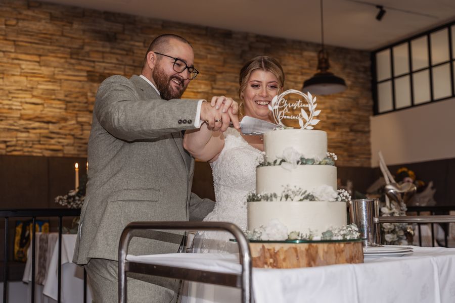 Christina und Dominik schneiden lachend ihre dreistöckige Hochzeitstorte an