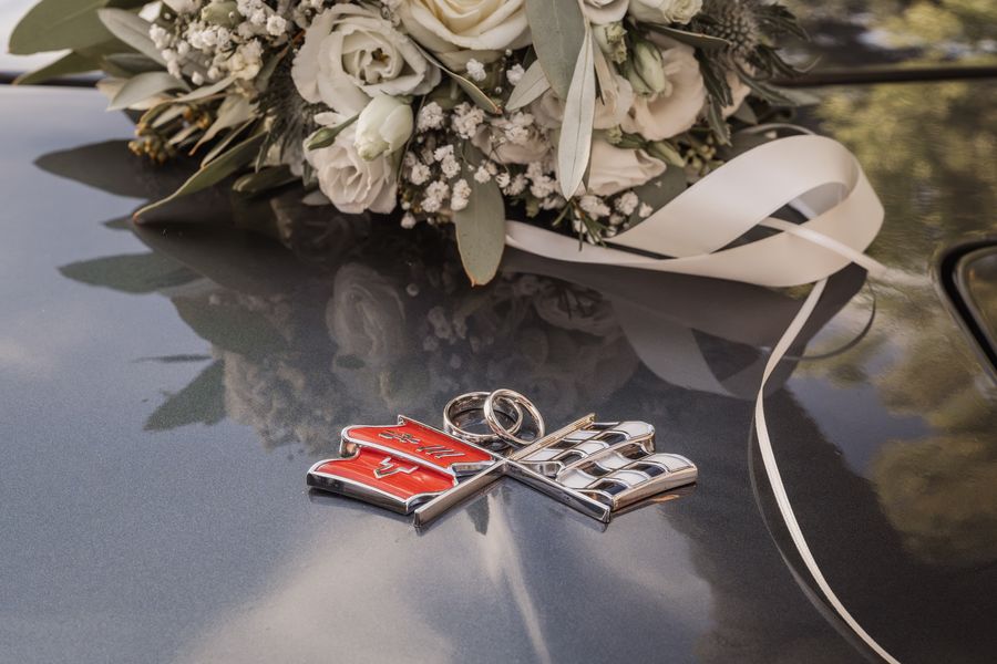 Die beiden Eheringe liegen auf dem Emblem der Corvette, dahinter der Brautstrauß auf der Motorhaube
