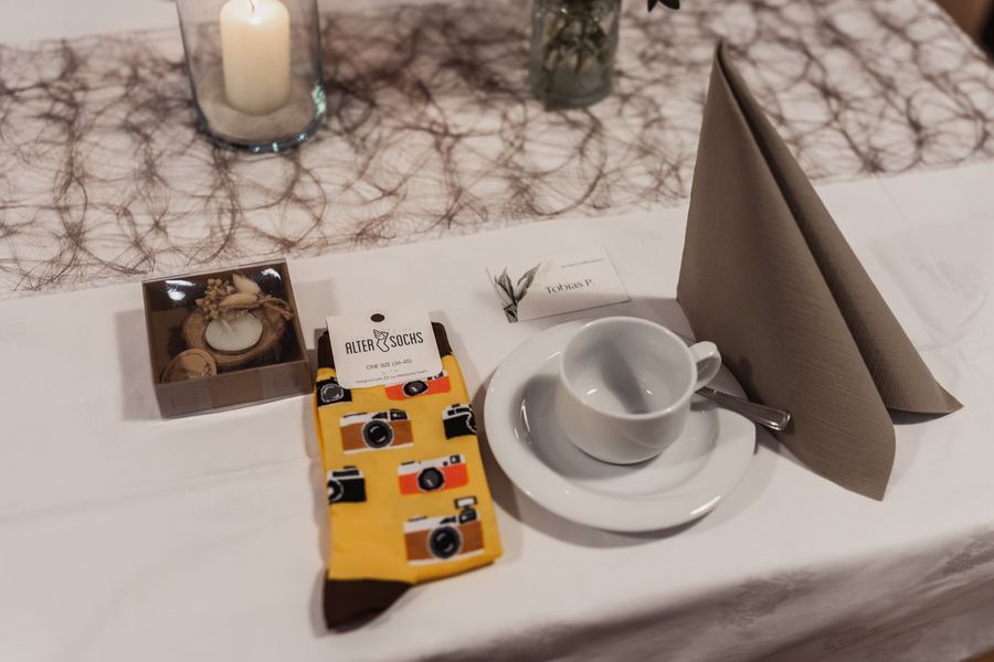 Gastgeschenk am Platz des Fotografen: Socken mit Kamera-Motiv neben Tasse und Namenskarte