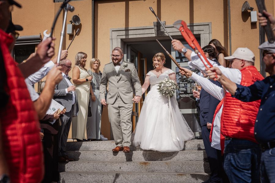 Christina und Dominik laufen nach der Trauung durch ein Spalier aus hochgehaltenem Werkzeug vor dem Standesamt