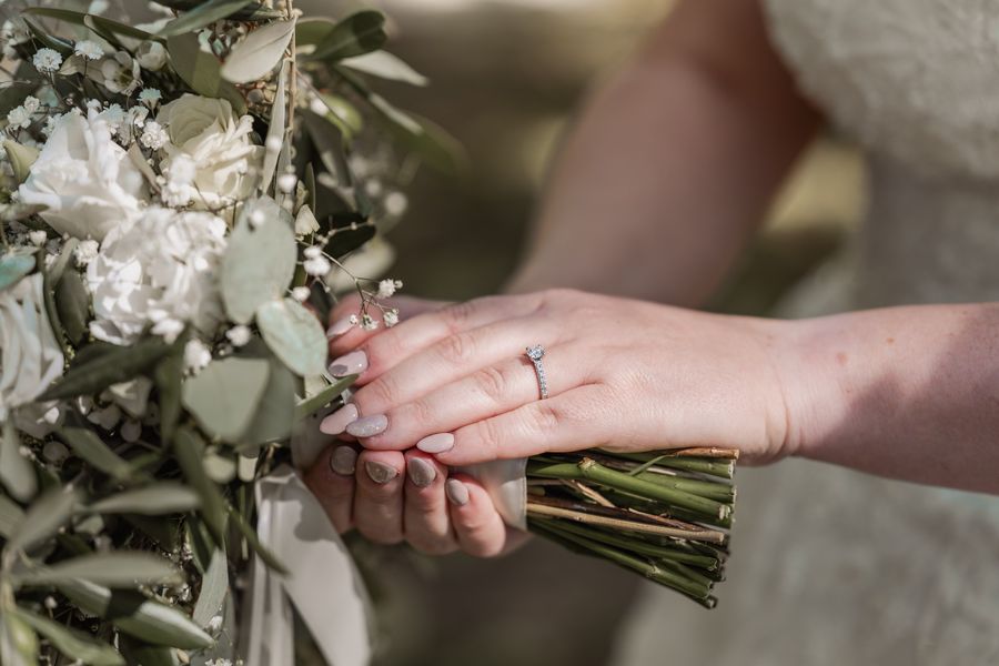 Christinas Hand mit Verlobungsring auf dem Brautstrauß aus weißen Rosen, Schleierkraut und Eukalyptus